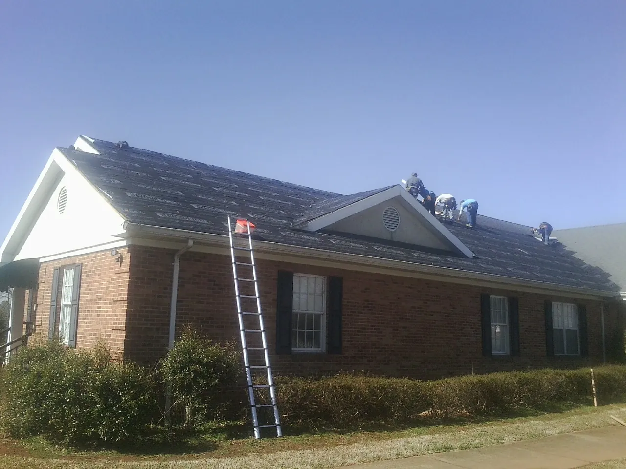 Crew tearing shingles off a brick ranch roof with a ladder set — Emergency Roof Repair work by our crew in Havelock
