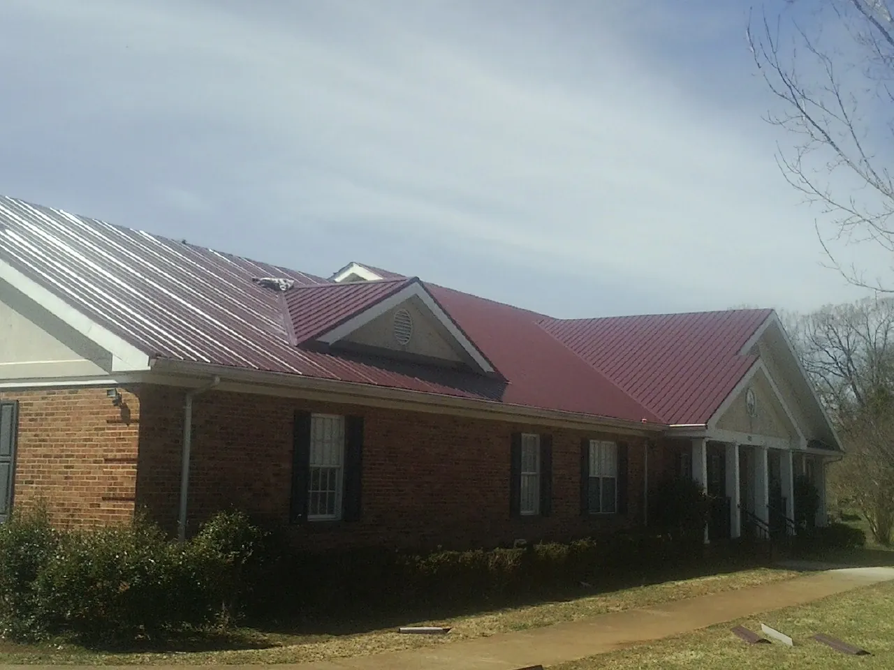 Red metal roof with gabled entries on a long brick building, from a Hail Damage Roof Repair job in Havelock
