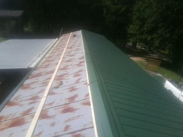 Old rusted panels beside newly installed green metal roofing — Wind Damage Roof Repair by Roofing Brothers in Havelock