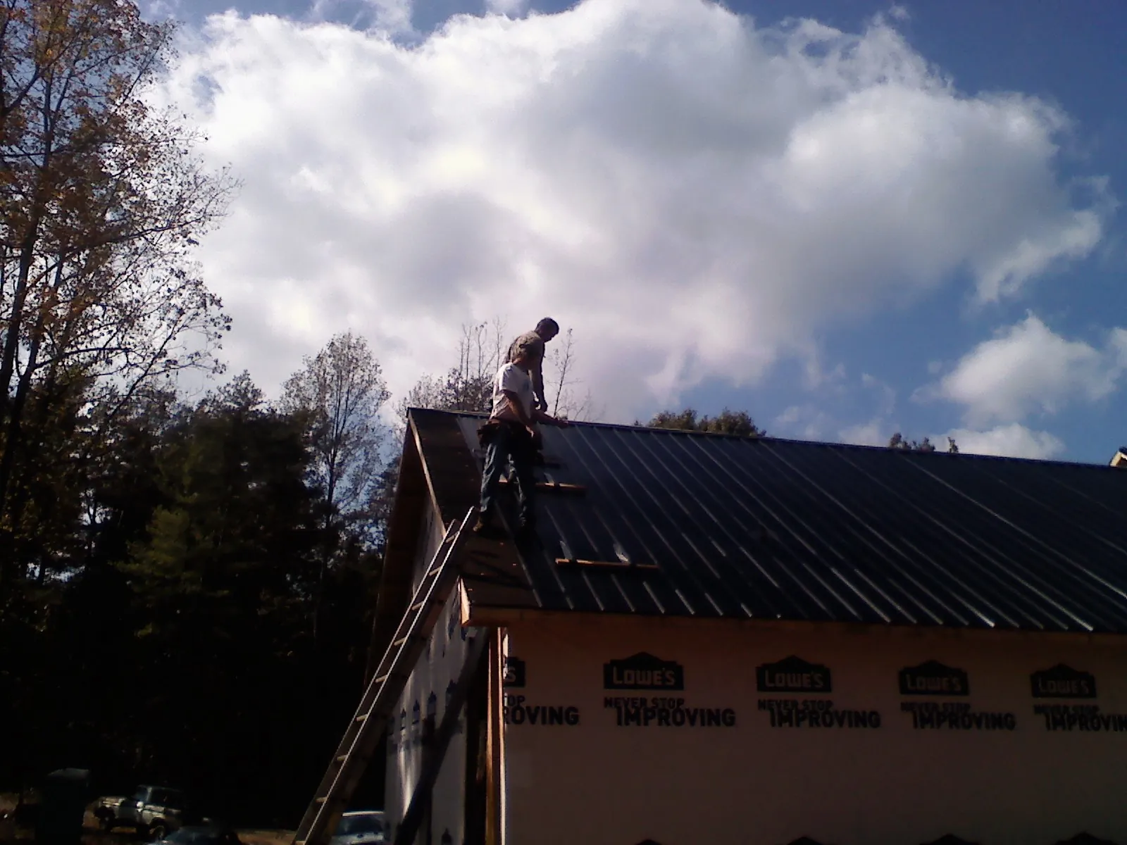 Roofer fastening dark metal panels high against a cloudy sky, from a Roof Inspection job in Havelock