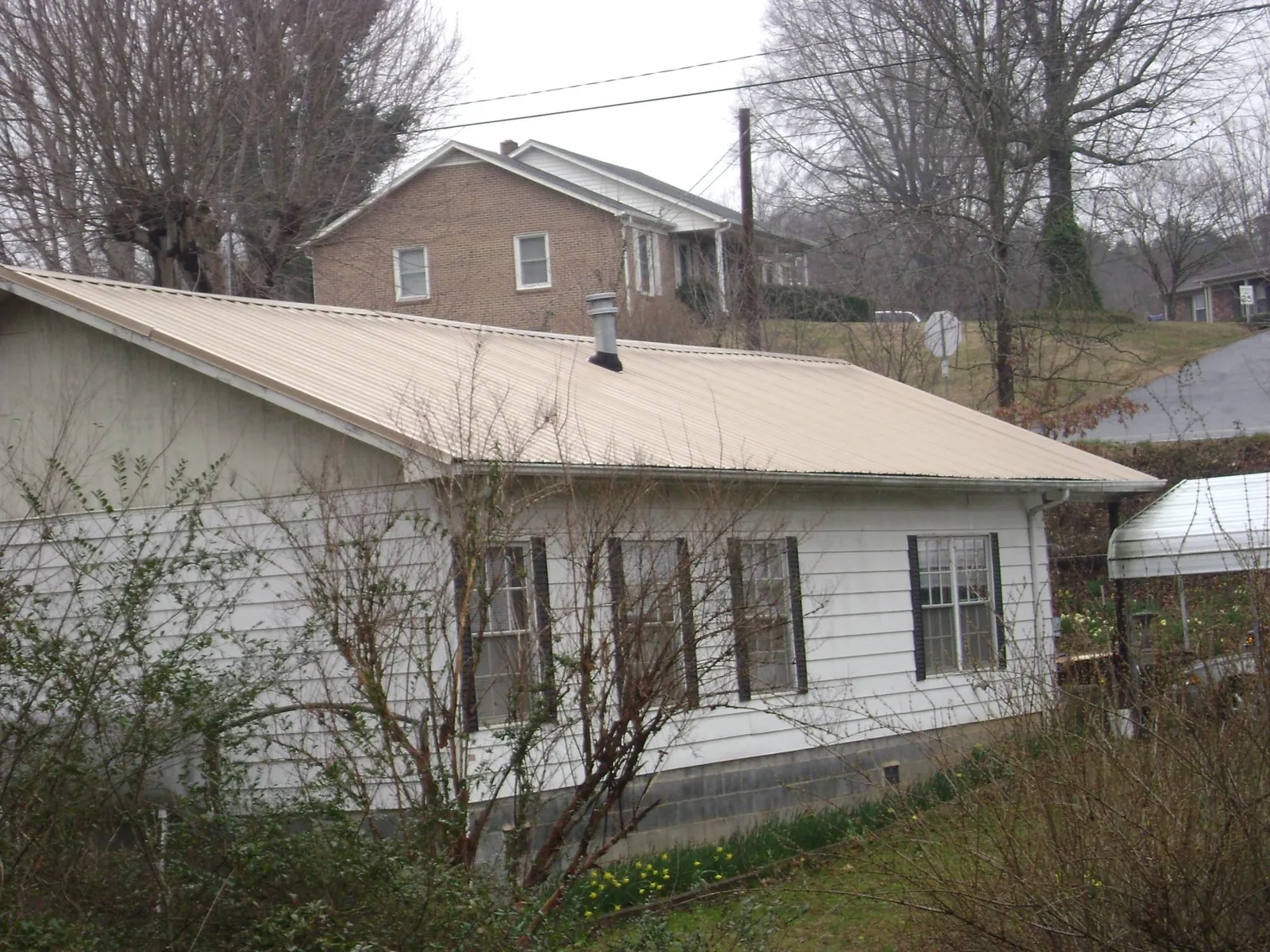 Tan metal roof on a white sided house set into a hillside — Commercial Roofing by Roofing Brothers in Havelock