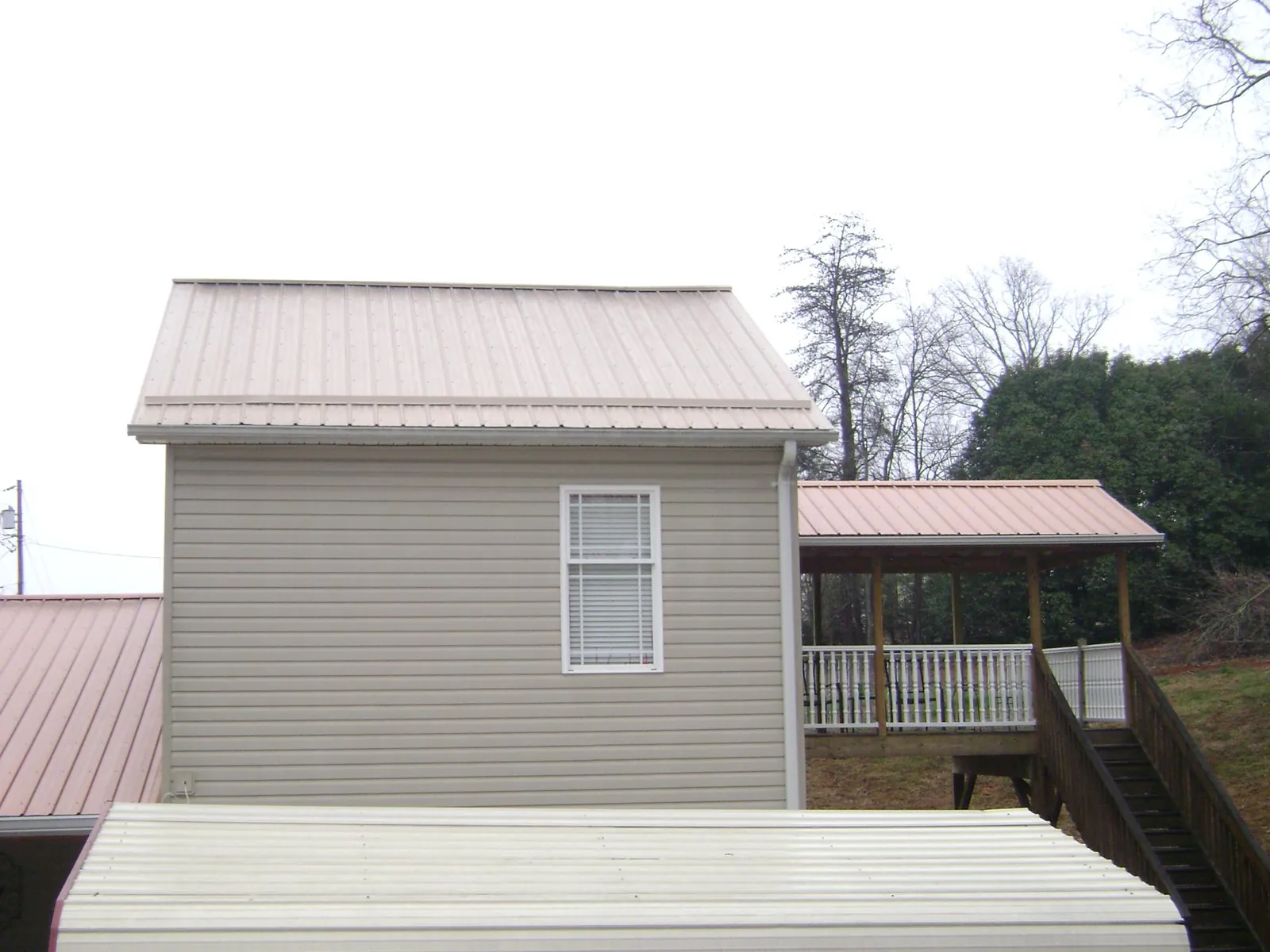 Tan metal roofs on a two story addition and attached porch, from a Roof Replacement job in Havelock